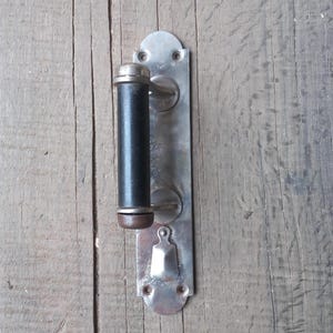 Könnte beinhalten: Ein silberner Türgriff mit einem schwarzen Holzgriff. Der Griff ist an einer Holztür montiert.