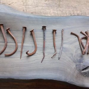 Może przedstawiać: Zbiór zardzewiałych gwoździ o różnych rozmiarach i kształtach, ułożonych na drewnianej powierzchni. Niektóre gwoździe są proste, inne zgięte lub zakrzywione. Gwoździe mają wygląd postarzałego.