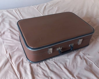 Puede incluir: Una maleta vintage marrón con ribetes negros y un asa negra.