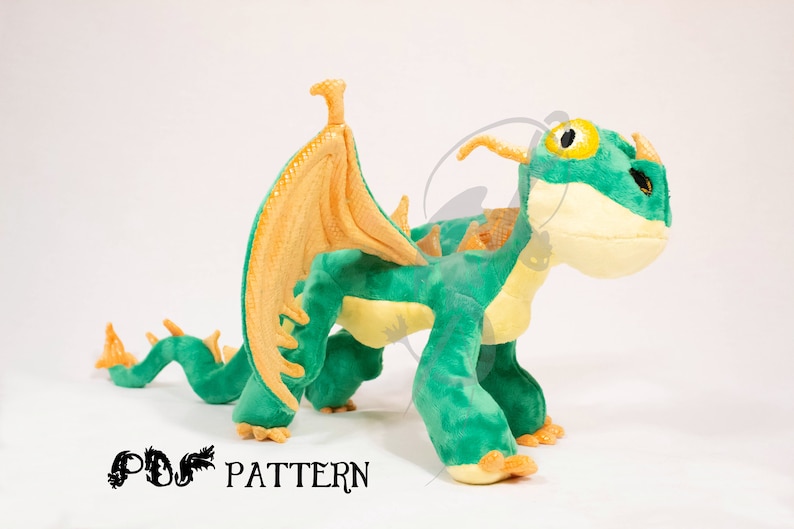 May include: Green and yellow plush dragon toy with orange wings and a long tail. The dragon has a large head with a yellow eye and a small horn on its nose.
