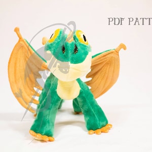 May include: Green and yellow plush dragon with orange wings. The dragon is standing on a white surface. PDF PATTERN.