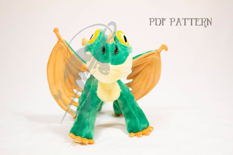 May include: Green and yellow plush dragon with orange wings. The dragon is standing on a white surface. PDF PATTERN.