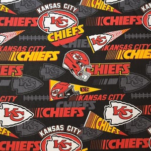 May include: Black fabric with a repeating pattern of the Kansas City Chiefs logo, the words "Kansas City Chiefs", and a football helmet. The logo is red, white, and yellow, and the helmet is red and white.