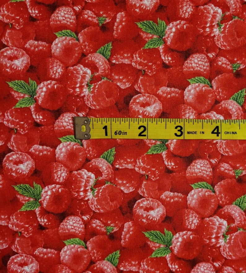 May include: Red fabric with a repeating pattern of red raspberries. A yellow measuring tape is partially visible at the bottom of the image. The tape reads "1 60 in 2 3 MADE IN 4 CHINA".