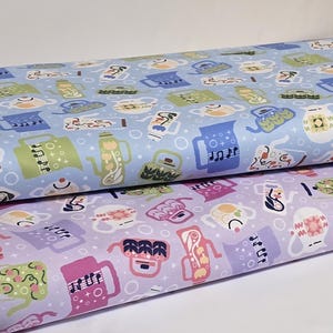 May include: Two rolls of fabric with a repeating pattern of teapots, mugs, and musical notes. The top roll is light blue, and the bottom roll is lavender. The teapots and mugs are in various colors, including green, pink, and yellow.
