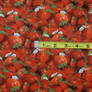 May include: Red fabric with a repeating pattern of strawberries and white flowers. A yellow measuring tape is placed across the fabric, showing measurements in inches.