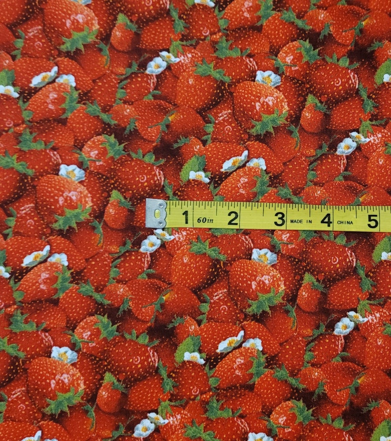 May include: Red fabric with a repeating pattern of strawberries and white flowers. A yellow measuring tape is placed across the fabric, showing measurements in inches.
