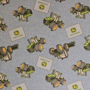 May include: A blue fabric with a repeating pattern of green John Deere tractors and logos. The tractors are green with black wheels and yellow accents. The logos are green with a yellow deer and the text "John Deere".
