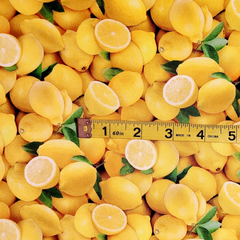 May include: A close-up of a fabric with a yellow lemon print. The fabric is covered in lemons of various sizes and shapes, some cut in half to show the inside.