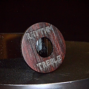 May include: A wooden knob with a hole in the centre. The knob is dark brown with a reddish hue and has the words "Rhythm Treble" engraved on it.