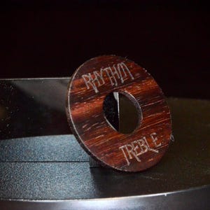 May include: A wooden knob with a hole in the center. The knob is dark brown with a reddish hue and has the words "Rhythm Treble" engraved on it.
