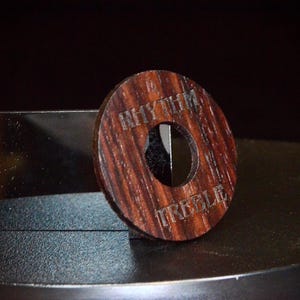 May include: A wooden knob with a hole in the centre. The knob is dark brown with a reddish hue and has the words "Rhythm Treble" engraved on it.