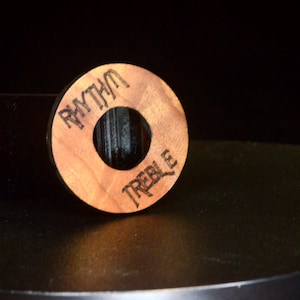 Puede incluir: Una perilla de madera con un agujero en el centro. La perilla está etiquetada con "Rhythm" y "Treble" en los lados opuestos.
