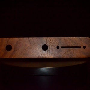 May include: A wooden guitar control plate with a dark brown finish. The plate has four holes and a long slot cut out.