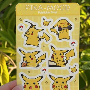 May include: A sheet of stickers featuring different expressions of Pikachu, a popular Pokemon character. The stickers are on a yellow background with a grid pattern and the text "PIKA-MOOD Potsticker Shop".