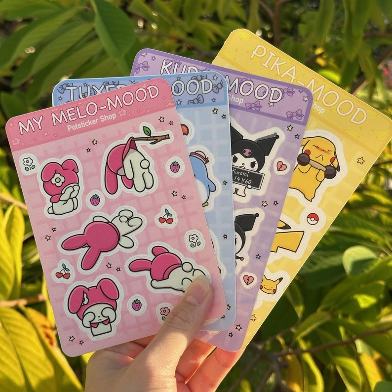 May include: Four sticker sheets with different themes. The first sheet features My Melo-Mood with pink and white characters. The second sheet features Kuromi with a black and white character. The third sheet features Pika-Mood with a yellow and black character. The fourth sheet features a blue and white character.