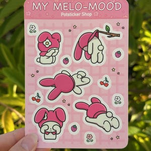 May include: A sheet of pink stickers featuring My Melody, a popular Japanese character. The stickers show My Melody in various poses, including sitting, lying down, and hanging from a branch. The stickers are decorated with stars, flowers, and strawberries.