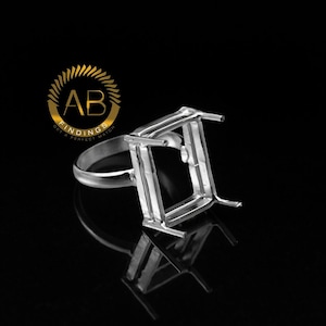 May include: A silver ring setting with a rectangular design, suitable for a gemstone. The ring is shown on a reflective black surface, with the logo "AB FINDINGS GET A PERFECT MATCH" in gold.