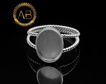 May include: Silver-toned ring with an oval setting and a twisted band design. The ring is displayed on a reflective black surface, showcasing its intricate details and design. The ring is a jewelry finding.