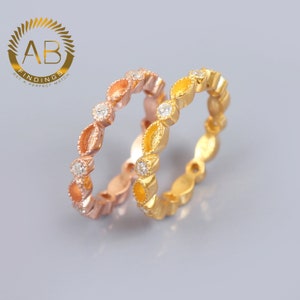 Pode incluir: Dois anéis delicados com acabamento dourado e ouro rosa. Cada anel apresenta uma fila de pequenas pedras transparentes engastadas em um design em forma de folha.