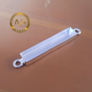 May include: Silver-toned pendant with two jump rings and a rectangular bezel for a flatback cabochon.  The pendant is approximately 1.5 inches long.