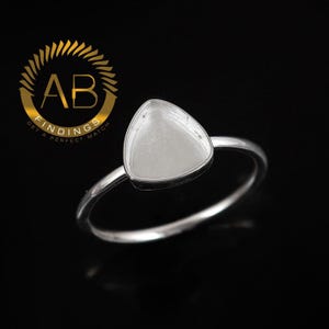 Op de afbeelding: Een zilveren ring met een driehoekige zetting. De ring heeft een gladde, gepolijste band en een bezel setting. De afbeelding bevat ook een gouden logo met de tekst "AB FINDINGS GET A PERFECT MATCH".