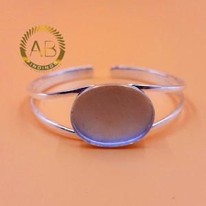 May include: A silver cuff bracelet with an oval setting. The bracelet features a double-band design and an open, adjustable style. The background is a solid orange colour. The logo "AB FINDINGS GET A PERFECT MATCH" is in the upper left corner.