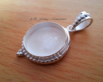 May include: A silver-colored pendant with a circular, recessed center. The pendant has a decorative beaded edge and a loop for a chain. The text "AB Findings Manufacturer" is printed on the surface.