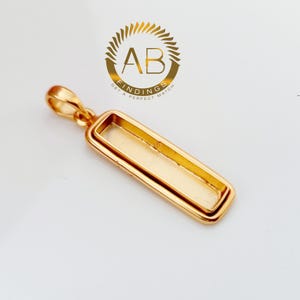 Peut inclure: Pendentif rectangulaire doré avec une boucle en haut pour une chaîne. Le pendentif a un cadre à double couche et une zone encastrée pour une pierre ou un motif. Le logo "AB FINDINGS GET A PERFECT MATCH" est en arrière-plan.