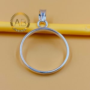 Peut inclure: Un pendentif argenté de forme circulaire. Il comporte une boucle en haut pour une chaîne. Le fond est de couleur jaune clair. Le pendentif est probablement destiné à la fabrication de bijoux.