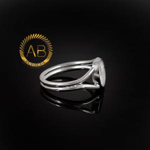 K&ouml;nnte beinhalten: Ein silberfarbener Metallring mit geteilter Ringschiene und einer runden Fassung f&uuml;r Steine. Der Ring wird neben einem goldenen, kreisf&ouml;rmigen Logo mit dem Text AB FINDINGS GET A PERFECT MATCH dargestellt.