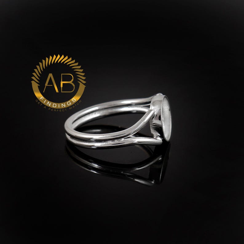 K&ouml;nnte beinhalten: Ein silberfarbener Metallring mit geteilter Ringschiene und einer runden Fassung f&uuml;r Steine. Der Ring wird neben einem goldenen, kreisf&ouml;rmigen Logo mit dem Text AB FINDINGS GET A PERFECT MATCH dargestellt.