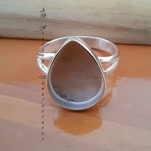 May include: A silver ring with a teardrop-shaped bezel setting. The bezel is empty and ready to be filled with a stone or other embellishment.