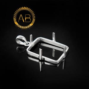 May include: A silver-colored rectangular pendant setting with four prongs and a loop for a chain. The pendant is designed to hold a gemstone or other decorative element. The background is black.