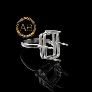 Peut inclure: Un sertissage de bague en argent avec un design rectangulaire, idéal pour une pierre précieuse. La bague est présentée sur une surface noire réfléchissante, avec le logo "AB FINDINGS" en or en arrière-plan.