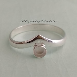 Pode incluir: Anel de prata com uma banda em forma de V e uma configuração de bezel redonda. O anel é projetado para segurar uma pedra ou outro enfeite.