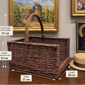 May include: A rectangular brown woven wicker basket with a single arched handle. The basket measures 48 cm in length, 27 cm in width, 25 cm in height without the handle, and 47 cm in total height including the handle, as indicated by text.