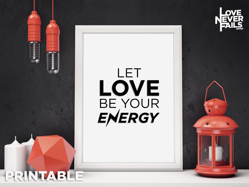 Puede incluir: Una impresi&oacute;n enmarcada en blanco con el texto "Let Love Be Your Energy" en letras negras. La impresi&oacute;n est&aacute; sobre una mesa con una linterna roja, dos velas y una forma geom&eacute;trica roja.