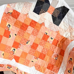 Pu&ograve; includere: Un quilt bianco con un design a patchwork con quadrati arancioni, neri e bianchi. Il quilt ha un design di gatto bianco e nero al centro ed &egrave; decorato con pois bianchi e neri.