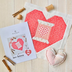 Puede incluir: Patrón de acolchado "Sew Loving" con un corazón rojo con un carrete de hilo y el texto "Sew Loving" sobre un fondo blanco. El patrón está rodeado por un borde blanco y un corazón rojo con un carrete de hilo.