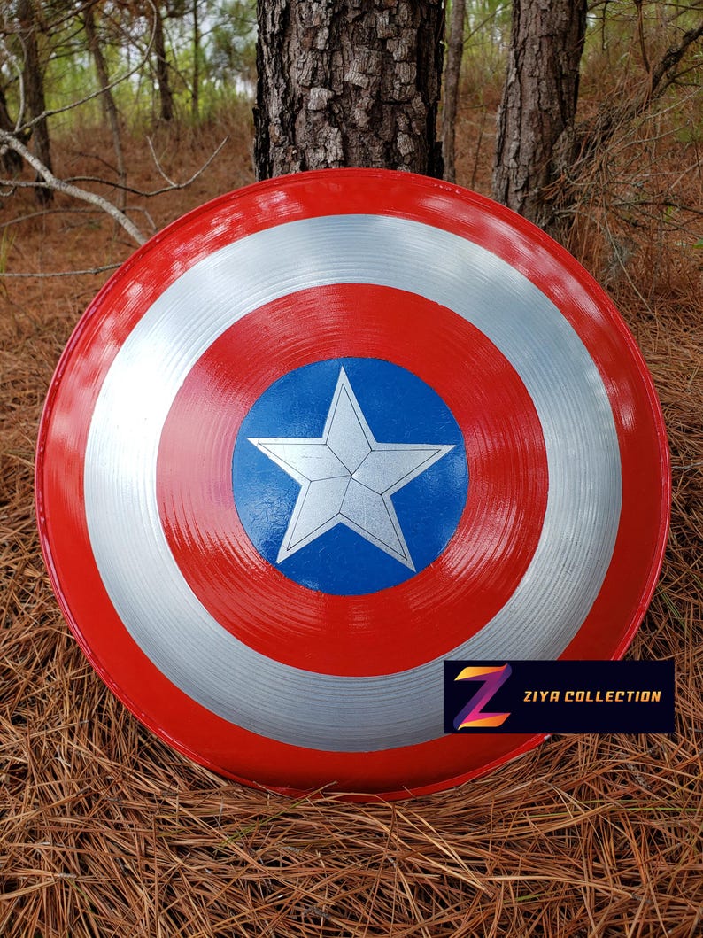 May include: A red, white, and blue shield with a star in the center, reminiscent of a superhero's emblem. The shield has a glossy finish and is displayed outdoors. The text "ZIYA COLLECTION" is visible on the lower right.