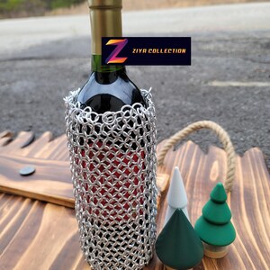 Op de afbeelding: Een fles rode wijn met een zilveren mali&euml;nkolder wijnfleshoes. De fles staat op een houten dienblad met drie decoratieve houten bomen. Het label luidt "ZIYA COLLECTION".