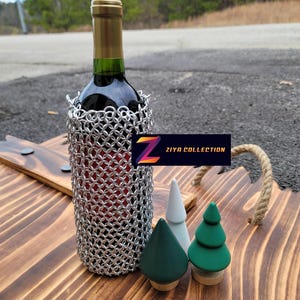 Op de afbeelding: Een fles rode wijn in een zilveren mali&euml;nkolder wijnfleshouder, gepresenteerd op een houten serveerblad met drie decoratieve houten boompjes. De tray heeft een touw handvat en de tekst "ZIYA COLLECTION".