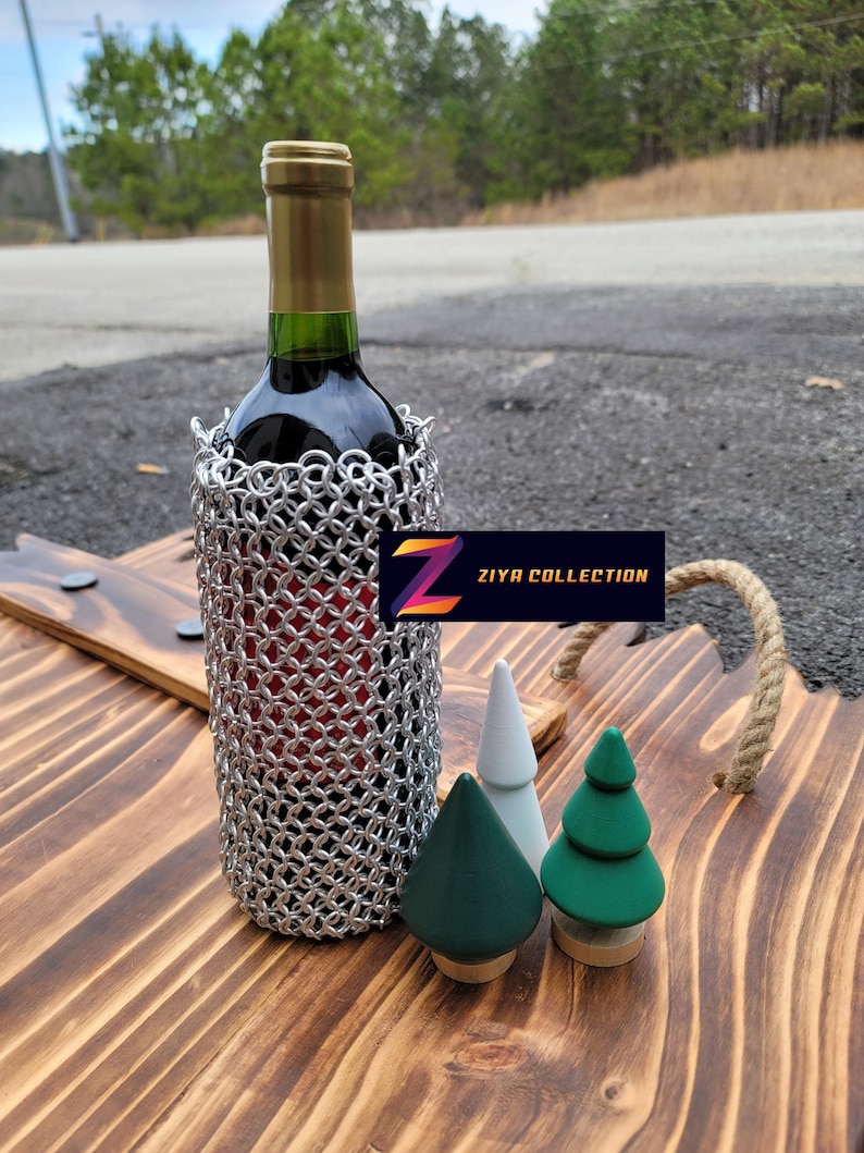 Op de afbeelding: Een fles rode wijn in een zilveren mali&euml;nkolder wijnfleshouder, gepresenteerd op een houten serveerblad met drie decoratieve houten boompjes. De tray heeft een touw handvat en de tekst "ZIYA COLLECTION".