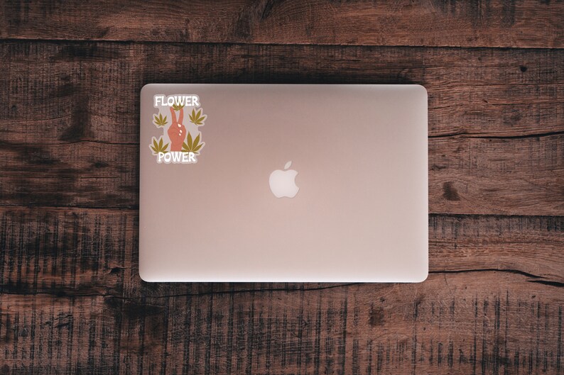 Puede incluir: Un ordenador port&aacute;til plateado con un logotipo de Apple blanco en la tapa. Una pegatina con el texto "Flower Power" y un signo de paz con hojas verdes est&aacute; en el lado izquierdo del port&aacute;til.