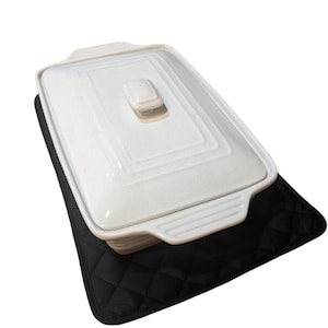 May include: White ceramic baking dish with a lid, sitting on a black quilted hot pad.