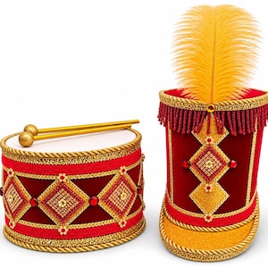 May include: A red velvet drum with gold trim, diamond-shaped sequin patterns, and two gold drumsticks, paired with a matching red velvet military-style hat featuring gold trim, red fringe, and a tall yellow feather plume on top.