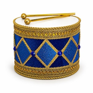 May include: A cylindrical drum featuring a deep blue velvet body decorated with a gold braided trim and a diamond pattern of blue glitter panels. The drum is accented with small blue circular gems and includes two gold drumsticks with textured ends.