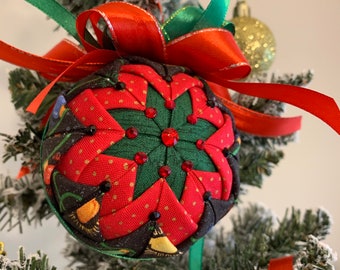 May include: A red, green, and black fabric Christmas ornament with a star design and red rhinestones. The ornament is hanging on a green Christmas tree with red and green ribbon.
