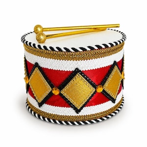 May include: A cylindrical drum featuring a red fabric body decorated with gold glitter diamond shapes, black trim, and white braided borders. The top surface is white, and two gold drumsticks with textured spherical ends rest on top.